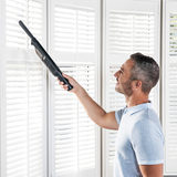 Image of a man cleaning the blinds with the hand held vacuum