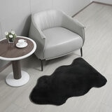 Black lambskin-style rug with an irregular, cloud-like shape and soft, fluffy texture on a light wooden floor