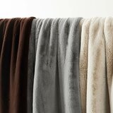 Three faux fur throws in brown, grey and beige hanging side by side