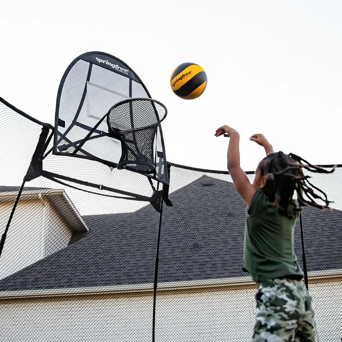 A lifestyle image of a child throwing a all into a hoop on the trampoline