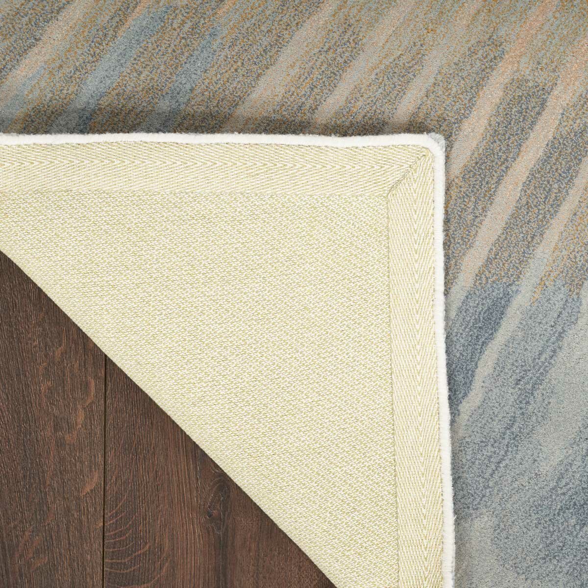 Gradient rug in blue, grey and beige, shown flipped to reveal a light beige herringbone backing with stitched edges.