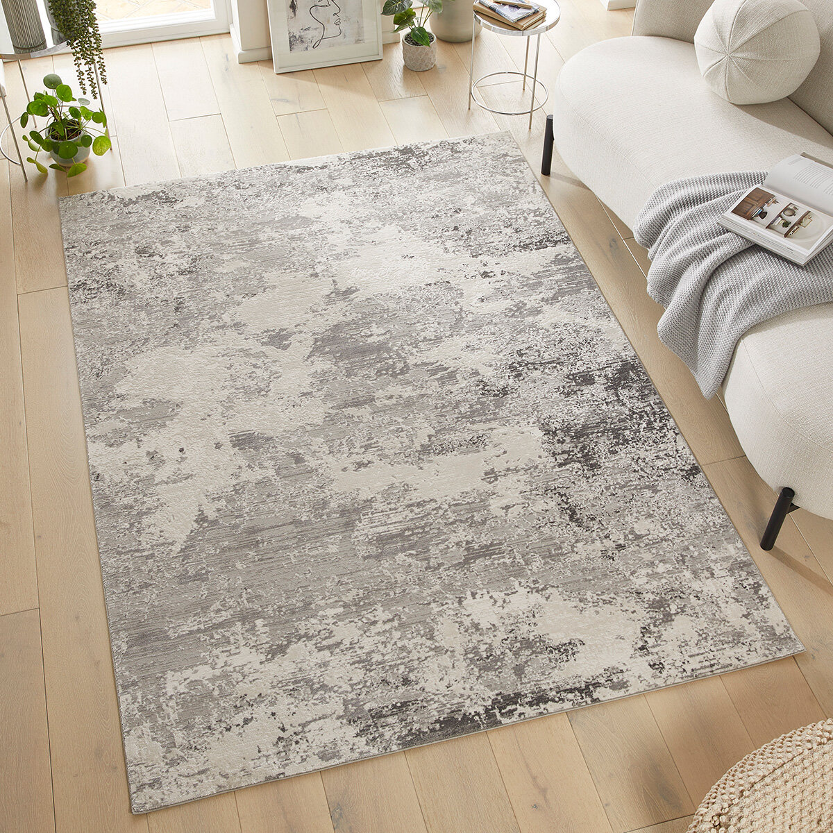 Large grey and cream rug with a distressed abstract pattern, placed in a modern living room with light wood flooring and minimal decor.