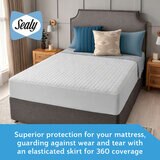 A fitted white mattress protector with a hexagonal quilted pattern on a neatly made bed in a modern bedroom
