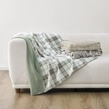 Plaid and floral throws in colours: Sage green, Taupe and black + white staged on a white sofa with minimalistic interior Plaid and floral throws in colours: Sage green, Taupe and black + white staged on a white sofa with minimalistic interior