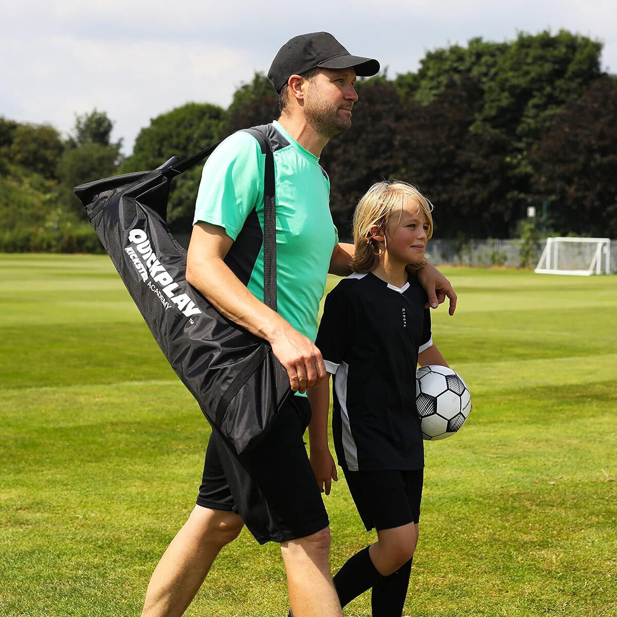 Lifestyle image of a man carrying the goal in the bag, his arm on the shoulder of a child walking next to him with the football