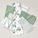 Eight green-themed tea towels arranged in a circle on a light surface, featuring solid, striped, checkered, and olive branch print designs Eight green-themed tea towels arranged in a circle on a light surface, featuring solid, striped, checkered, and olive branch print designs
