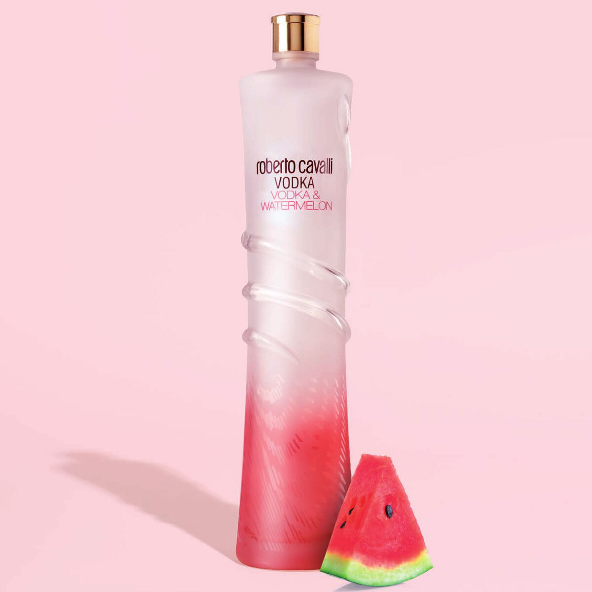 Lifestyle image of bottle in front of pink background with watermelon