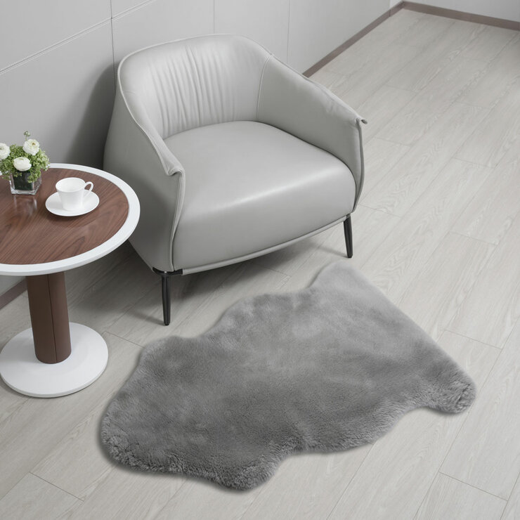 Grey lambskin-style rug with an irregular, cloud-like shape and soft, fluffy texture on a light wooden floor