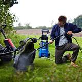 Lifestyle imahe of pressure washeer being used to clean lawnmower