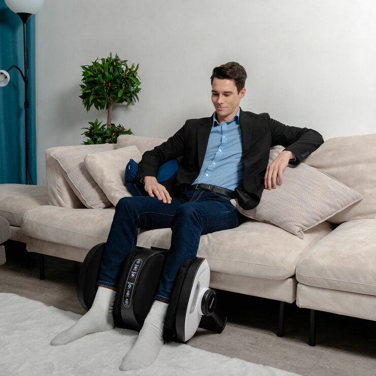 Lifestyle image of model usingt the massager on their calves in living room