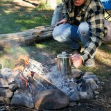 A lifestyle image of someone putting the percolator onto a campfire