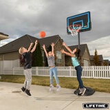 Lifestyle image of three children playing basketball with the Lifetime 32 Inch Youth Portable Basketball Hoop in the background