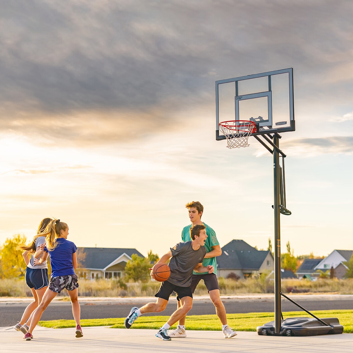 Lifestyle image of four people playing basketball with the 52 inch basketball hoop in the background Lifestyle image of four people playing basketball with the 52 inch basketball hoop in the background