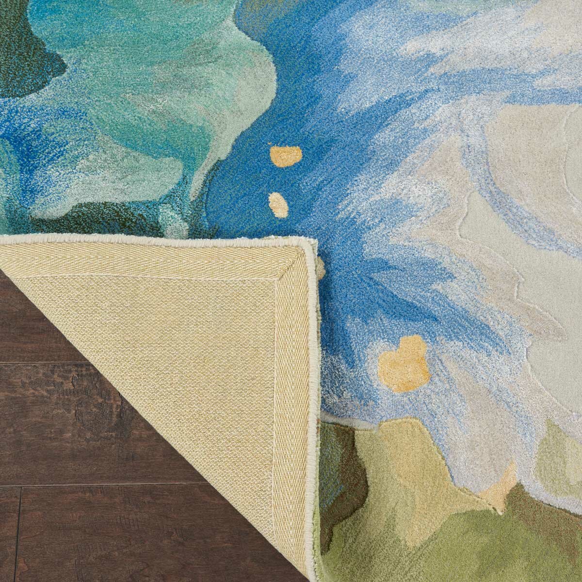 Corner of a patterned rug folded to show the plain beige underside. The top has a colourful abstract design in blue, green, and yellow.